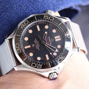 Alternative view of The Seamaster 007 Edition features a 42mm titanium case with a black aluminum diving bezel adorned with brown markings, offering exceptional water resistance. Its black dial, also crafted from aluminum alloy, incorporates brown markings and bears the British Royal Property "Broad Arrow" triangular arrowhead emblem at the 6 o'clock position.Powered by the Master-certified bidirectional automatic 8806 movement, this 007 edition features a solid caseback engraved with the 007 emblem and a series of codes: "0552" signifies naval service, "9237697" denotes a diver's watch, and the letter "A" indicates a screw-down crown.The final "62" signifies the year 1962 when the film Dr. No was released. The watch comes with a titanium Milanese mesh bracelet with folding clasp and a NATO strap. The box is made of canvas and houses an imported ETA mechanical movement. Royal continues to deliver premium quality.